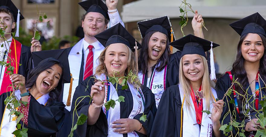 Excited students in their caps and gowns proudly hold up their ivy at SPU