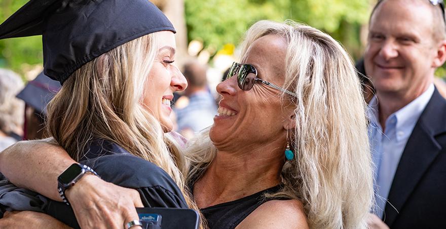 A mother hugs her daughter who is dressed in her cap and gown at SPU